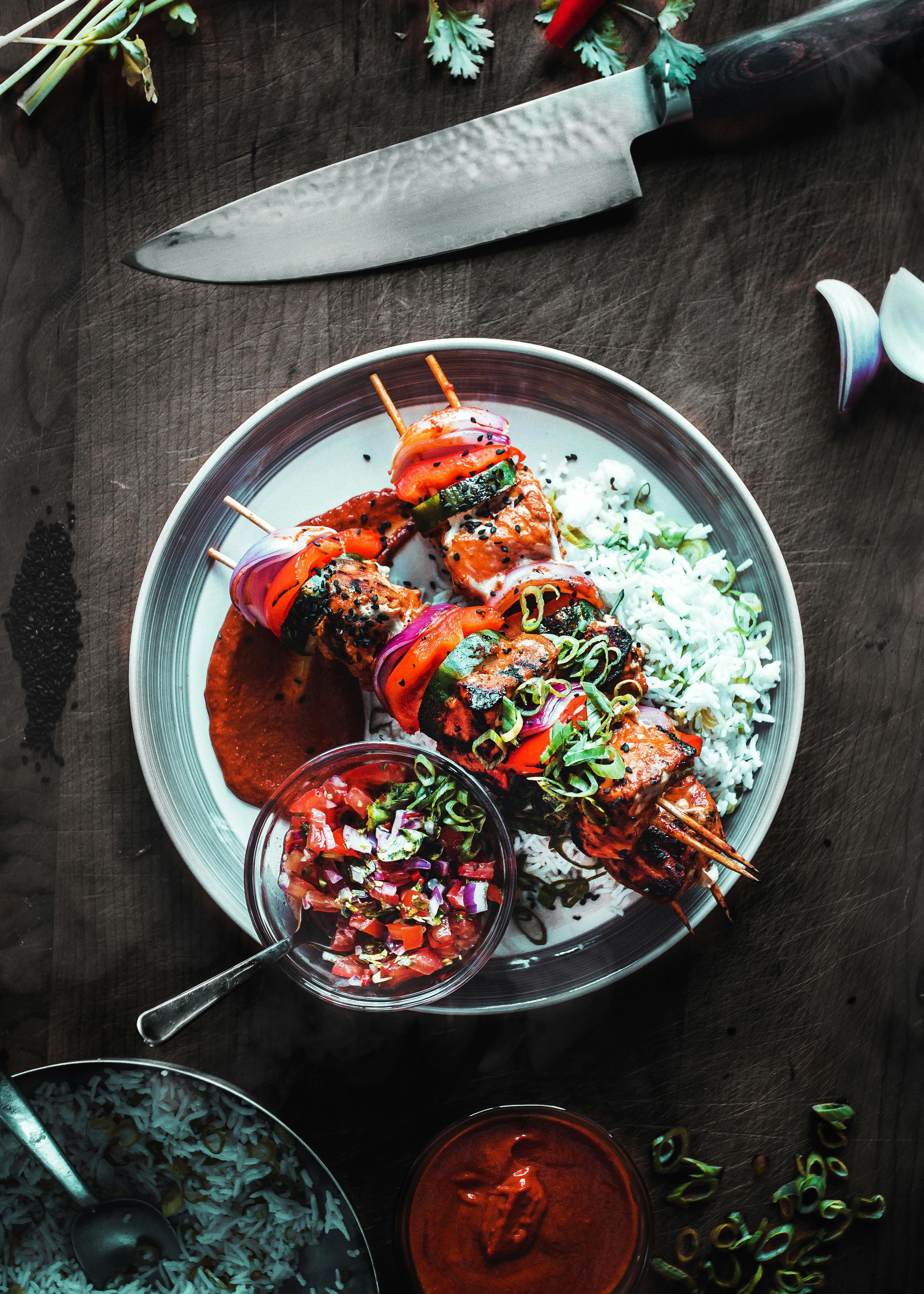Delicious grilled skewers with rice and salsa served on a wooden table.