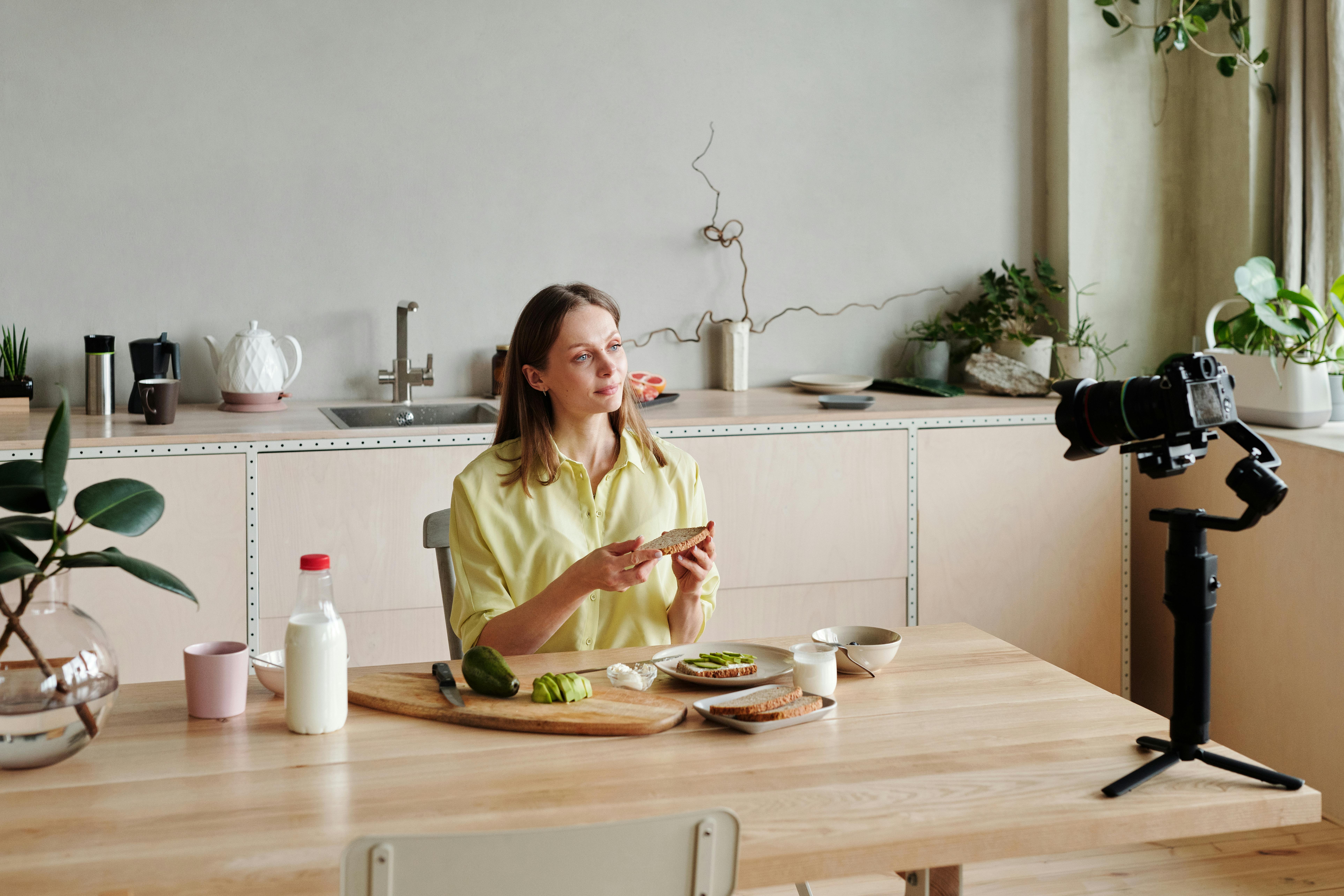 Woman in yellow filming a culinary vlog in a modern kitchen.