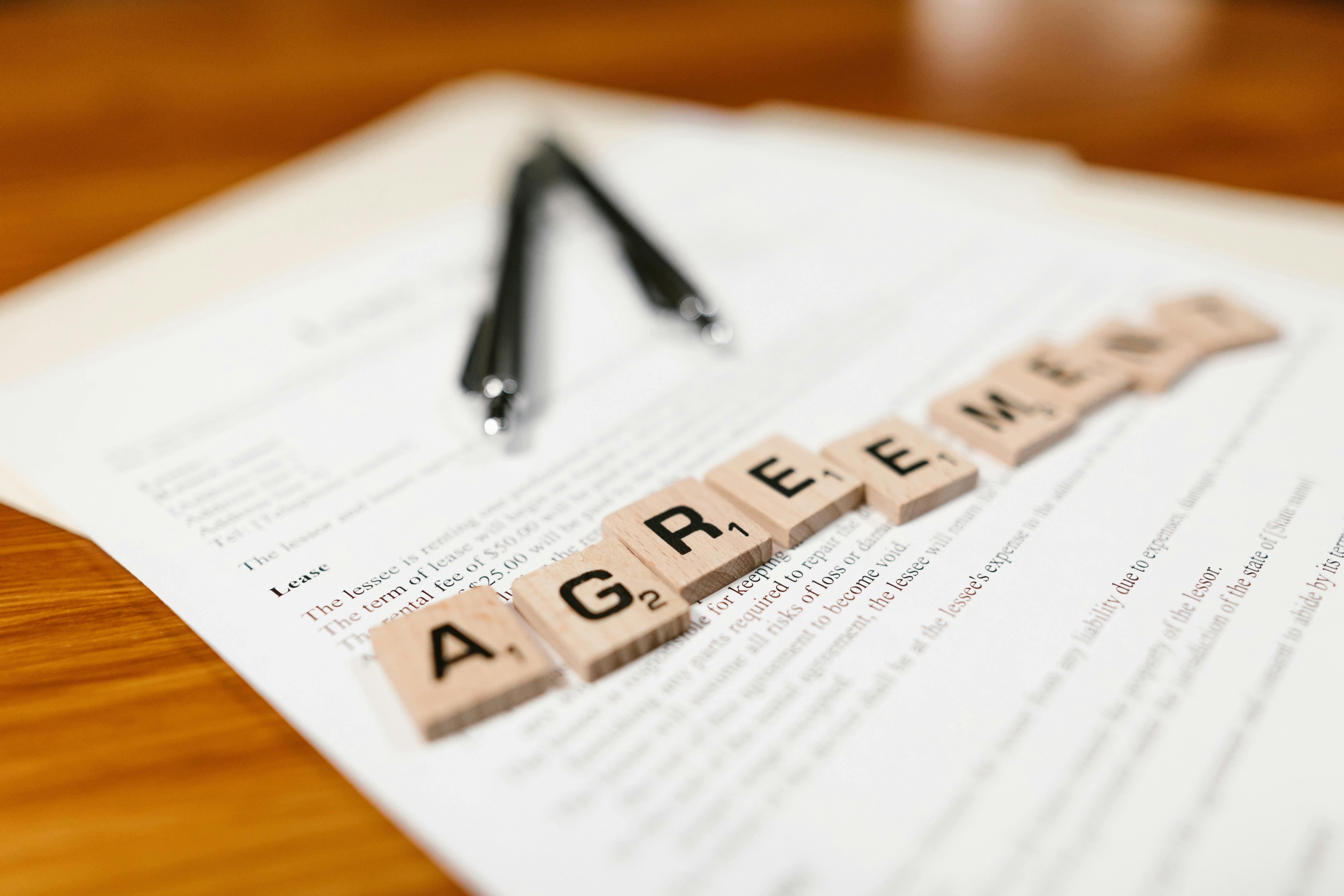 Scrabble tiles spelling 'AGREEMENT' on a lease document, emphasizing contractual themes.