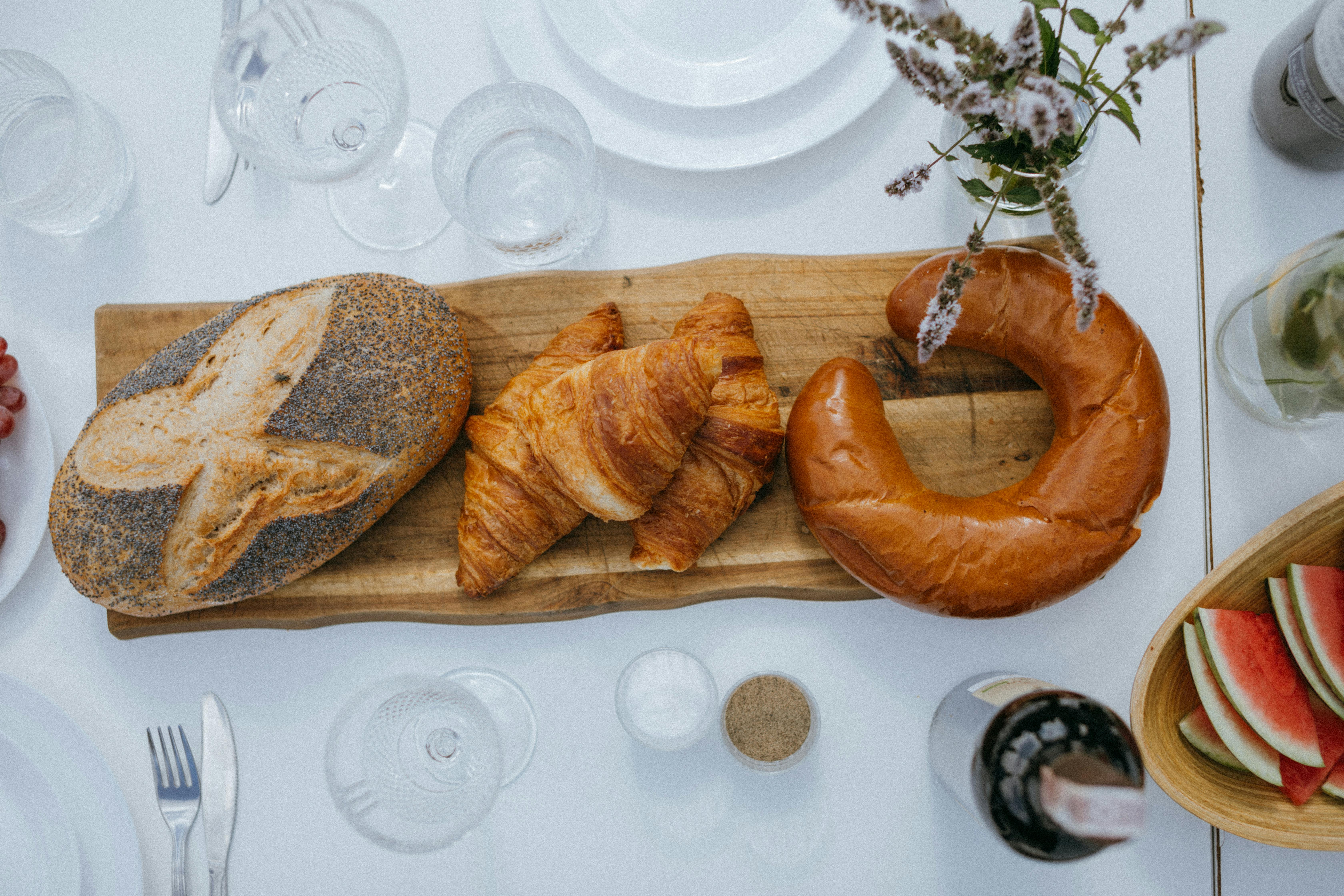 An inviting breakfast display featuring a variety of breads and croissants on a wooden board, set on a white table.